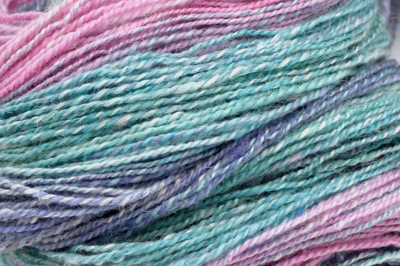 A close up view of a one of a kind, hand dyed gradient skein of multicolored Light Pink, Sky Blue, Seafoam Green, Grey, and Lavender self-striping wool Yarn.