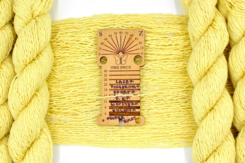 A skein of dk weight Bright Yellow Yarn recycled by hand from unwanted sweaters draped over a Yarn weight tool