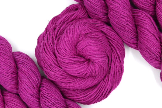 A skein of Vegan, Bright Fuchsia Pink, 55% Ramie, 45% Cotton, Worsted weight Yarn recycled by hand from unwanted sweaters swirled attractively in the center of the frame.