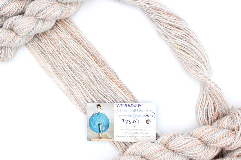 A one of a kind, hand dyed gradient skein of variegated skein of multicolored Cream, Dusky Pink, and Grey self-striping wool Yarn draped diagonally across the frame, so you can really see the color play.