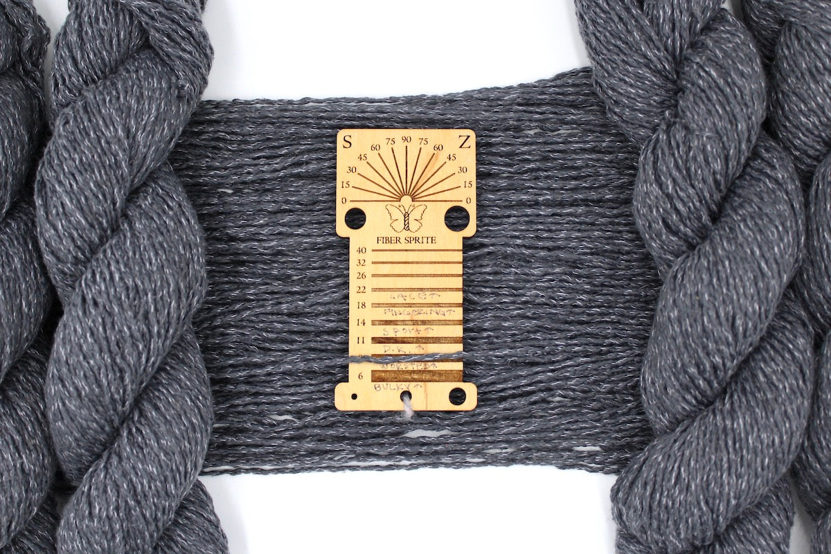 A skein of Worsted weight Grey Yarn recycled by hand from unwanted sweaters draped over a Yarn weight tool