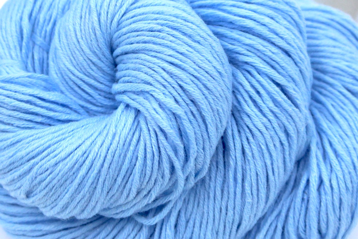 A close up shot of a skein of baby blue Yarn recycled by hand from unwanted sweaters beautifully coiled in the center of the frame