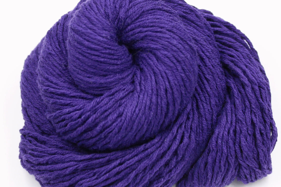 A close up shot of a skein of Vegan, Purple, 62% Cotton, 38% Acrylic, DK weight Yarn recycled by hand from unwanted sweaters beautifully coiled in the center of the frame.
