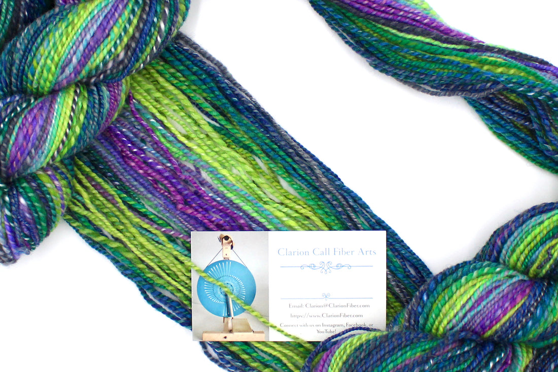 A one of a kind, Worsted weight, hand dyed Gradient skein of multicolored Navy Blue, Forest Green, Lime Green, Baby Blue, Purple, and Magenta, Ombre self-striping Wool, Bamboo, and Silk Yarn draped diagonally across the frame, so you can really see the color play.