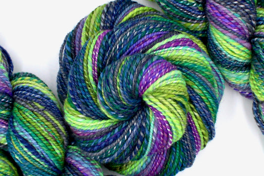 A one of a kind, Worsted weight, hand dyed Gradient skein of multicolored Navy Blue, Forest Green, Lime Green, Baby Blue, Purple, and Magenta, Ombre self-striping Wool, Bamboo, and Silk Yarn coiled attractively in the center of the frame.