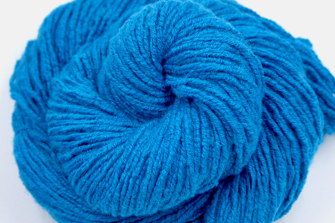 A close up shot of a skein of Bright Sky Blue, Wool, Acylic, Nylon, Angora, Worsted weight Yarn recycled by hand from unwanted sweaters beautifully coiled in the center of the frame.