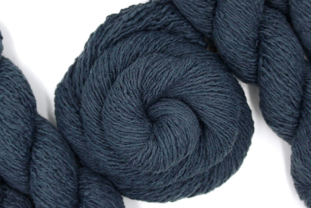 A skein of dark grey sport weight Yarn recycled by hand from unwanted sweaters swirled attractively in the center of the frame.