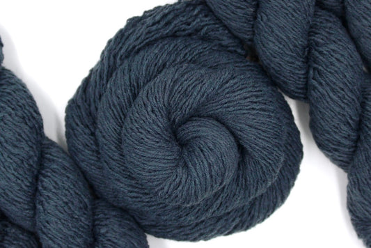 A skein of dark grey sport weight Yarn recycled by hand from unwanted sweaters swirled attractively in the center of the frame.
