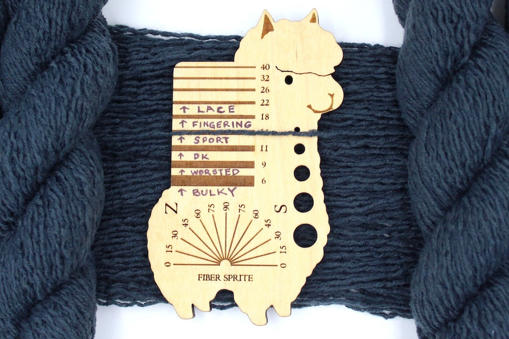 A skein of dark grey sport weight Yarn recycled by hand from unwanted sweaters draped over a Llama shaped Yarn weight tool.