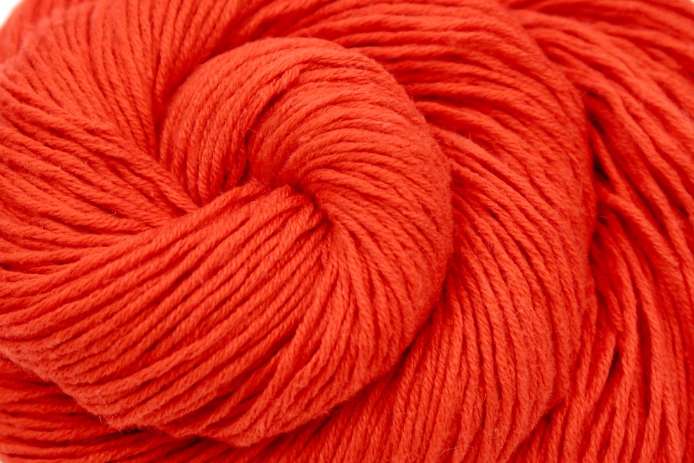 A close up shot of a skein of Bright Orange, Fingering weight Yarn recycled by hand from unwanted sweaters beautifully coiled in the center of the frame.