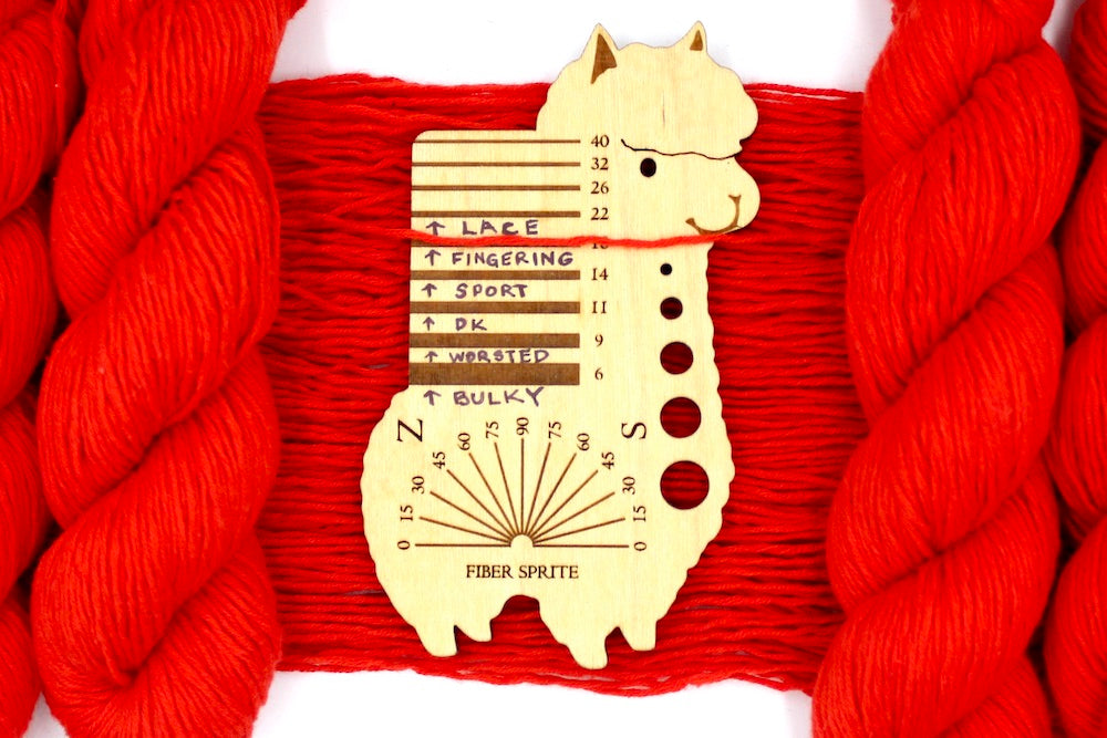 A skein of Bright Orange, Fingering weight Yarn recycled by hand from unwanted sweaters draped over a Llama shaped Yarn weight tool.