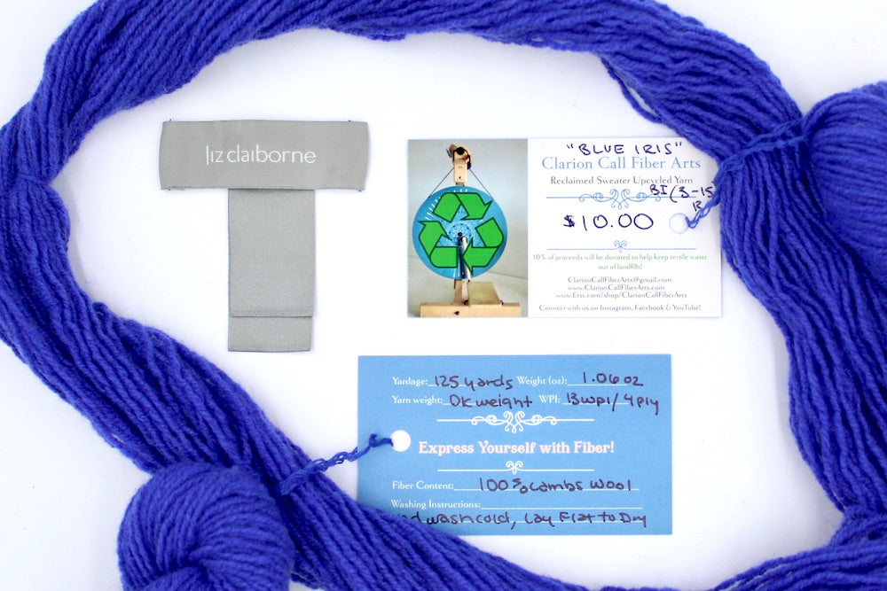 A skein of Violet, Dk weight yarn encircling the sweater tags it was recycled from, as well as the hand written yarn tags detailing the specs of this upcycled yarn to help you make your next project!