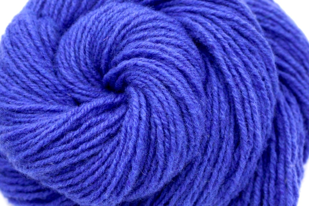 A close up shot of a skein of Violet, Dk weight Yarn recycled by hand from unwanted sweaters beautifully coiled in the center of the frame.
