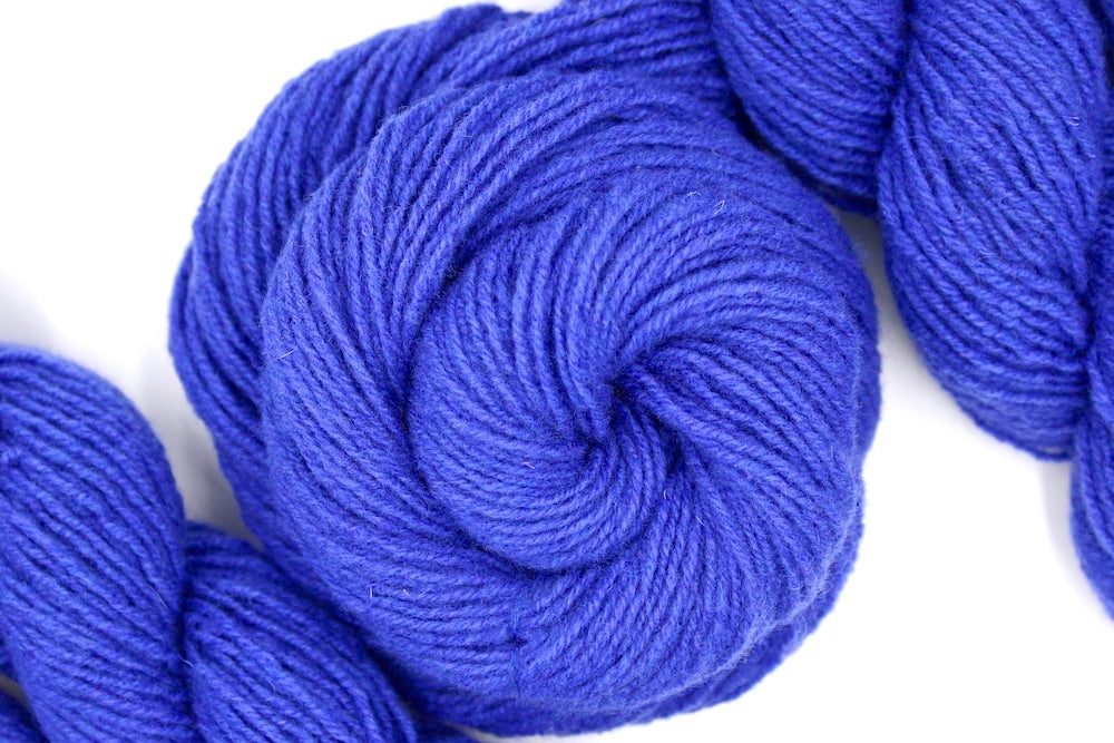 A skein of Violet, Dk weight Yarn recycled by hand from unwanted sweaters swirled attractively in the center of the frame.