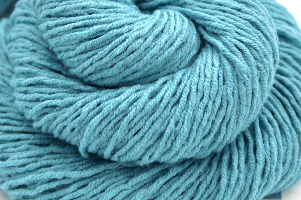 A close up shot of a skein of Light Blue, Dk weight Yarn recycled by hand from unwanted sweaters beautifully coiled in the center of the frame.
