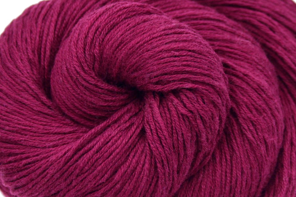 A close up shot of a skein of Maroon, Fingering weight Yarn recycled by hand from unwanted sweaters beautifully coiled in the center of the frame.