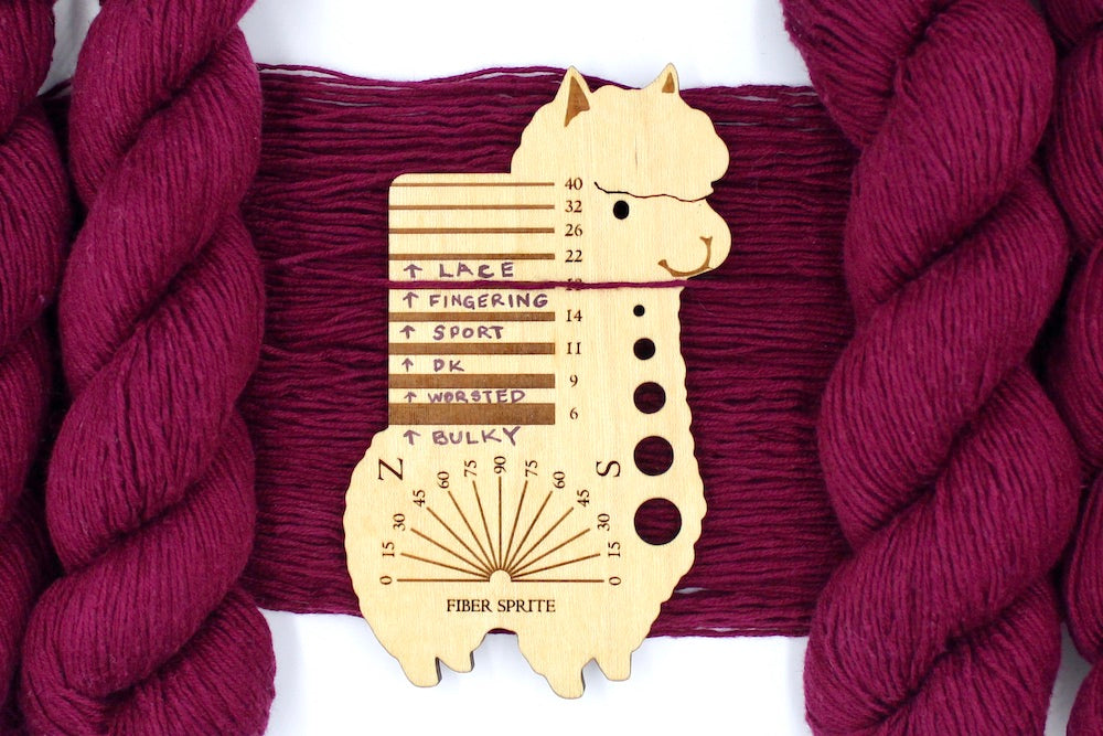 A skein of Maroon, Fingering weight Yarn recycled by hand from unwanted sweaters draped over a Llama shaped Yarn weight tool.