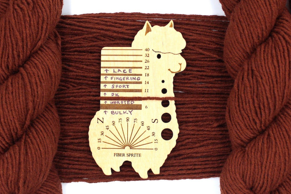 A skein of Reddish brown, Worsted weight Yarn recycled by hand from unwanted sweaters draped over a Llama shaped Yarn weight tool.