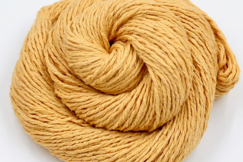 A close up shot of a skein of Vegan, Orangey Yellow, 60% Cotton, 40% Acrylic, DK weight Yarn recycled by hand from unwanted sweaters beautifully coiled in the center of the frame.