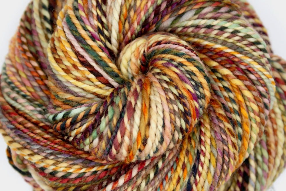 A close up view of a one of a kind, DK Weight, hand dyed variegated skein of multicolored Orange, Rust, Green, and Gold, self-striping superwash wool Yarn.