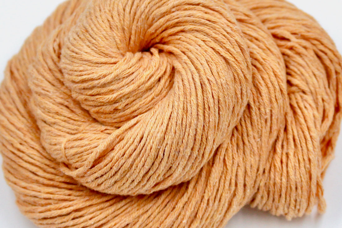 A close up shot of a skein of Vegan, Light Orange Peach, 100% Cotton, DK weight Yarn recycled by hand from unwanted sweaters beautifully coiled in the center of the frame.