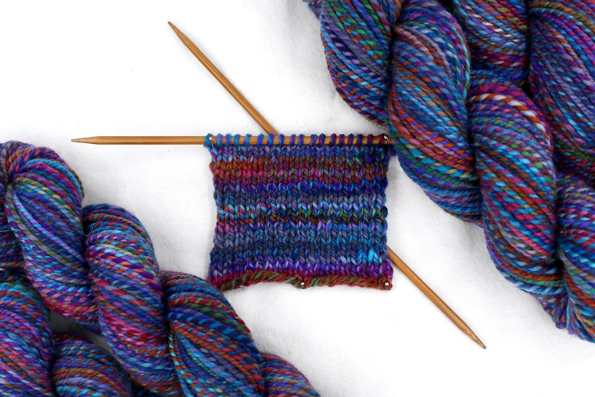 A sample swatch knitted from a one of a kind, hand dyed Variegated skein of multicolored Rainbow self-striping wool Yarn.