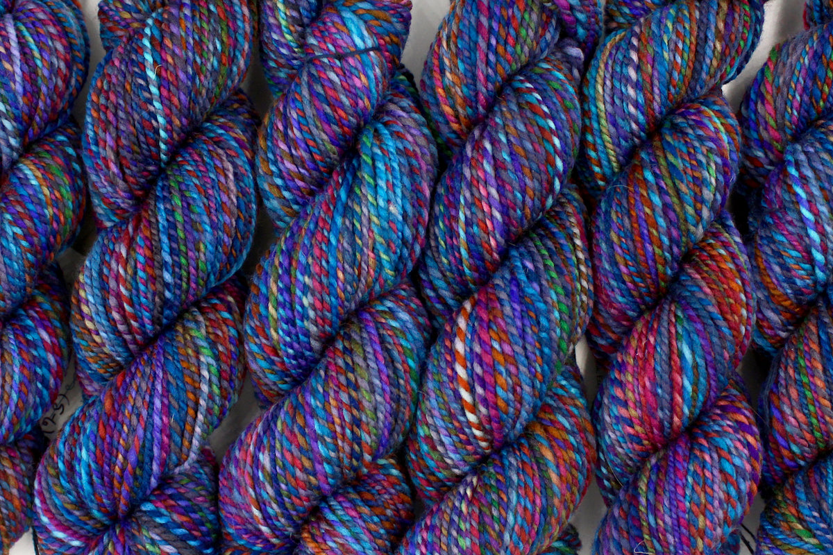 Six one of a kind, hand dyed Variegated skeins of multicolored Rainbow self-striping wool Yarn lined up side by side.