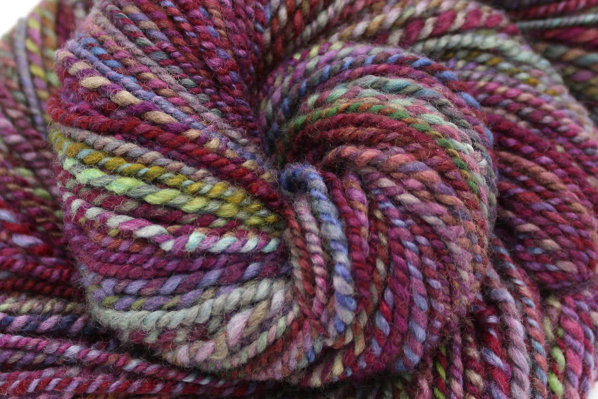 A close up view of a one of a kind, hand dyed Variegated skein of multicolored Maroon, Pink, Cornflower Blue, and Lime Green self-striping wool Yarn.