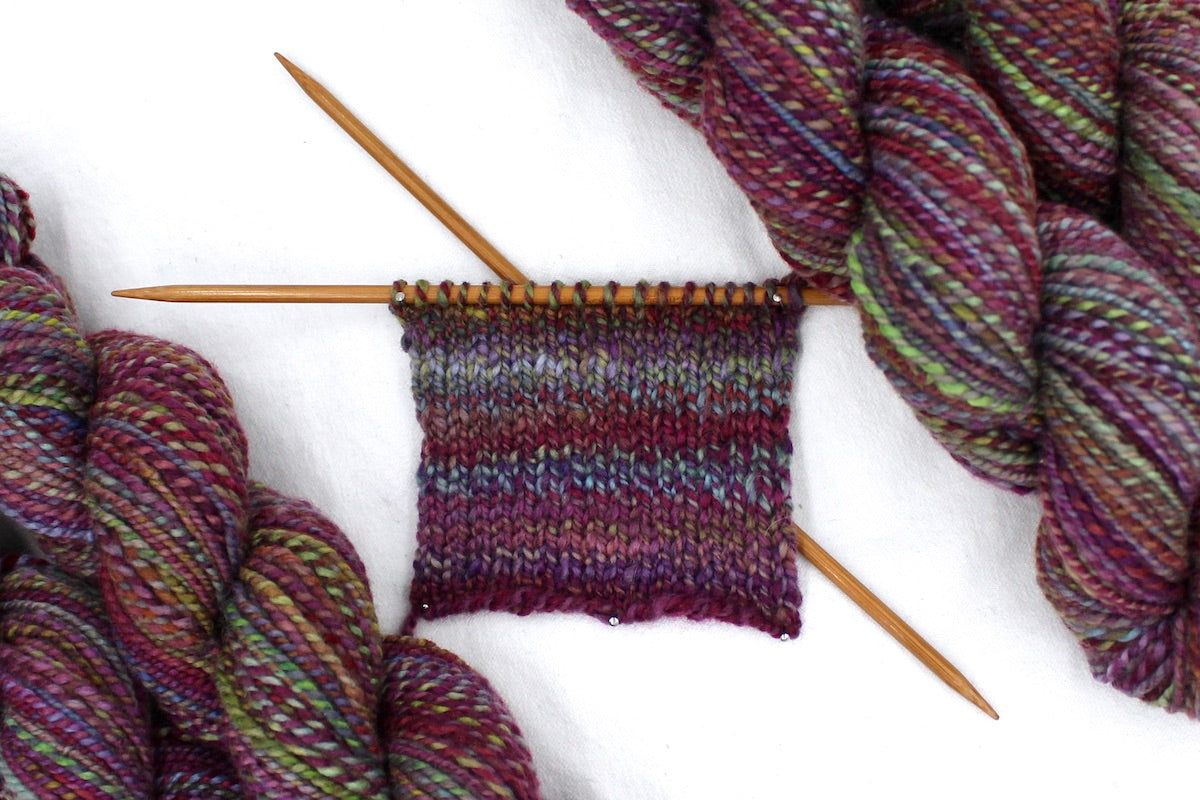 A sample swatch knitted from a one of a kind, hand dyed Variegated skein of multicolored Maroon, Pink, Cornflower Blue, and Lime Green self-striping wool Yarn.