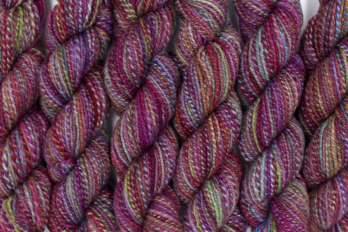 Six one of a kind, hand dyed Variegated skein of multicolored Maroon, Pink, Cornflower Blue, and Lime Green self-striping wool Yarn lined up side by side.