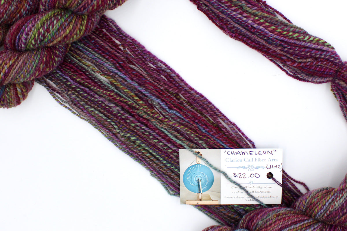 A one of a kind, hand dyed Variegated skein of multicolored Maroon, Pink, Cornflower Blue, and Lime Green self-striping wool Yarn draped diagonally across the frame, so you can really see the color play.