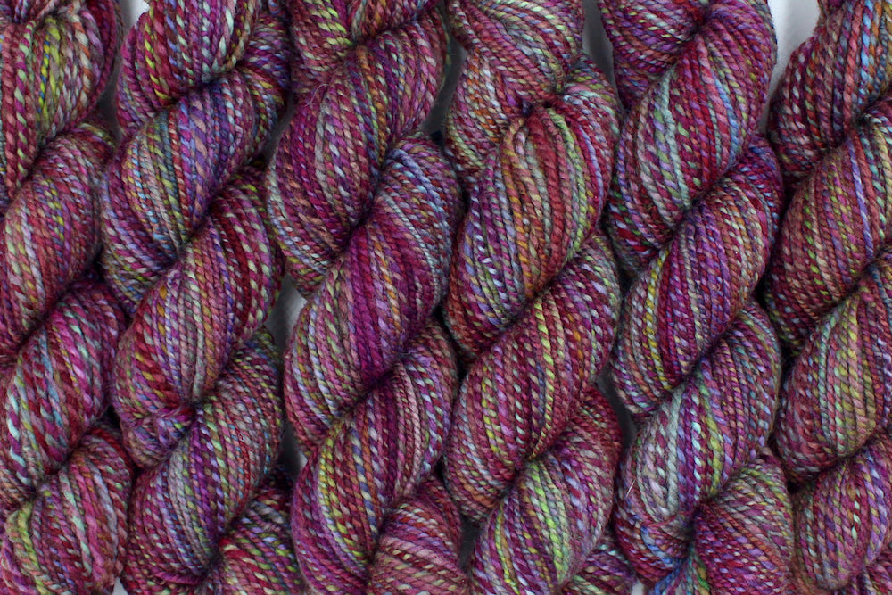 Six one of a kind, Dk Weight, hand dyed Variegated skeins of self striping Maroon, Pink, Cornflower Blue, and Lime Green Yarn, made of 100% Hand Dyed Merino Wool lined up side by side.