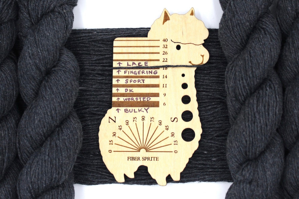 A skein of Dark Grey, Fingering weight Yarn recycled by hand from unwanted sweaters draped over a Llama shaped Yarn weight tool.