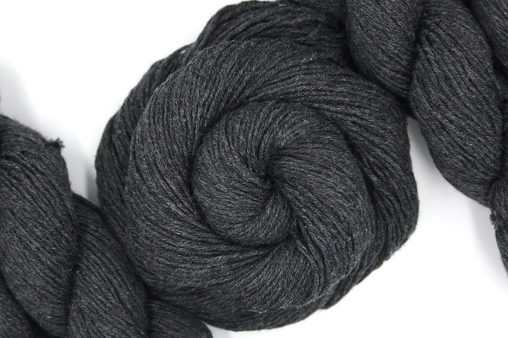 A skein of Dark Grey, Fingering weight Yarn recycled by hand from unwanted sweaters swirled attractively in the center of the frame.