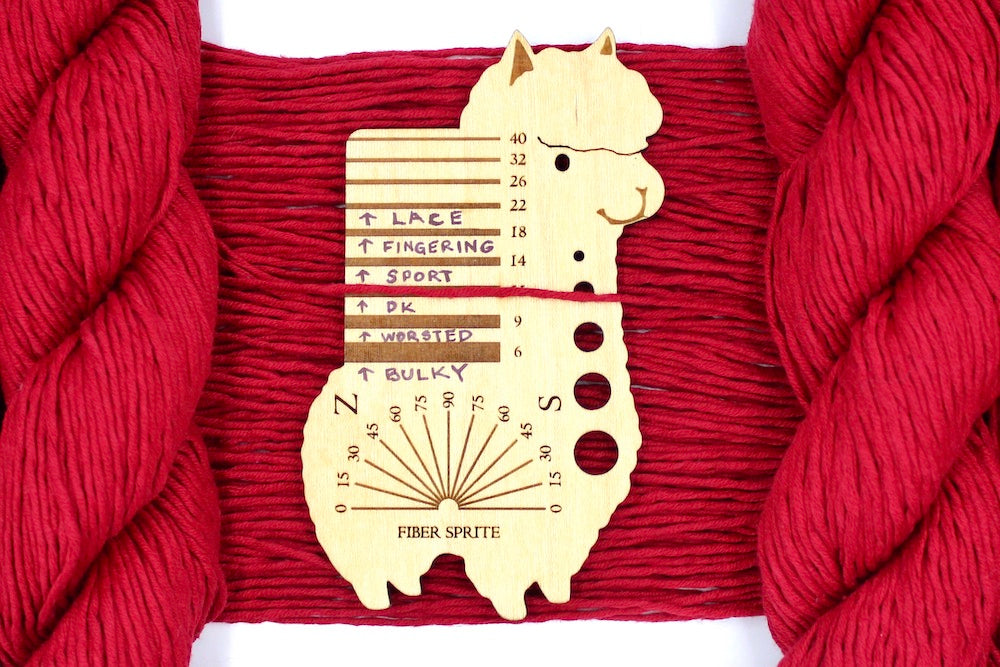 A skein of Ruby Red, Dk weight Yarn recycled by hand from unwanted sweaters draped over a Llama shaped Yarn weight tool.