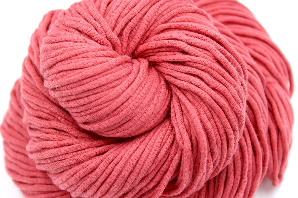 A close up shot of a skein of Coral Pink, Worsted weight Yarn recycled by hand from unwanted sweaters beautifully coiled in the center of the frame.