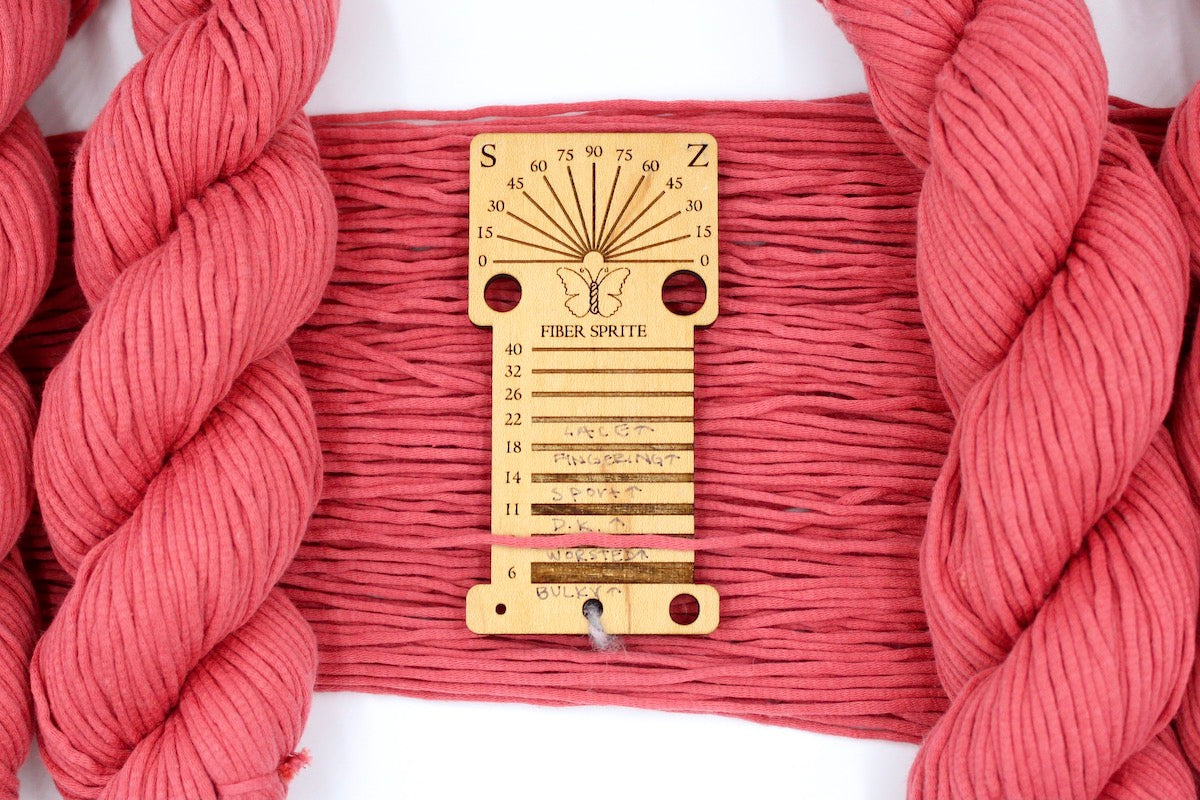 A skein of Coral Pink, Worsted Yarn recycled by hand from unwanted sweaters draped over a Llama shaped Yarn weight tool.