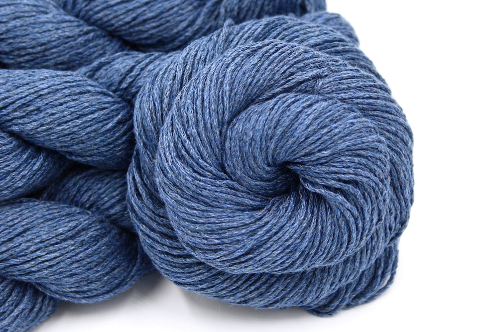 A close up shot of a skein of Cornflower Blue, Dk weight Yarn recycled by hand from unwanted sweaters beautifully coiled in the center of the frame.