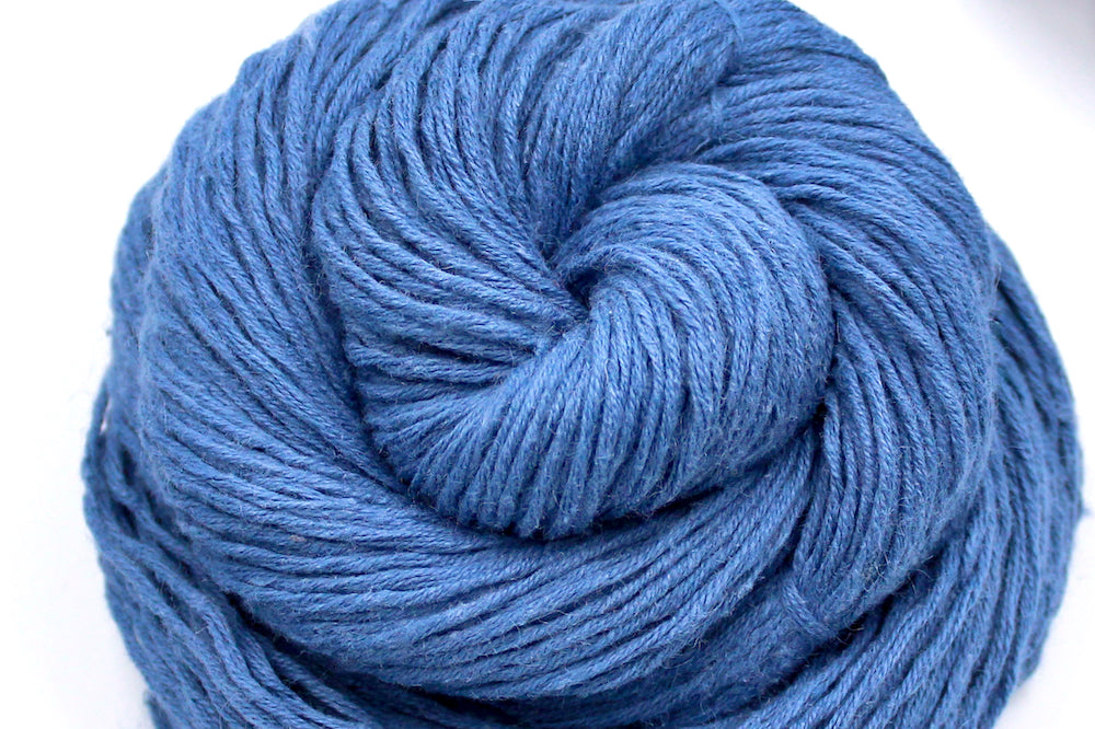 A close up shot of a skein of Vegan, Cornflower Blue, 55% Ramie, 45% Cotton, Worsted weight Yarn recycled by hand from unwanted sweaters beautifully coiled in the center of the frame.