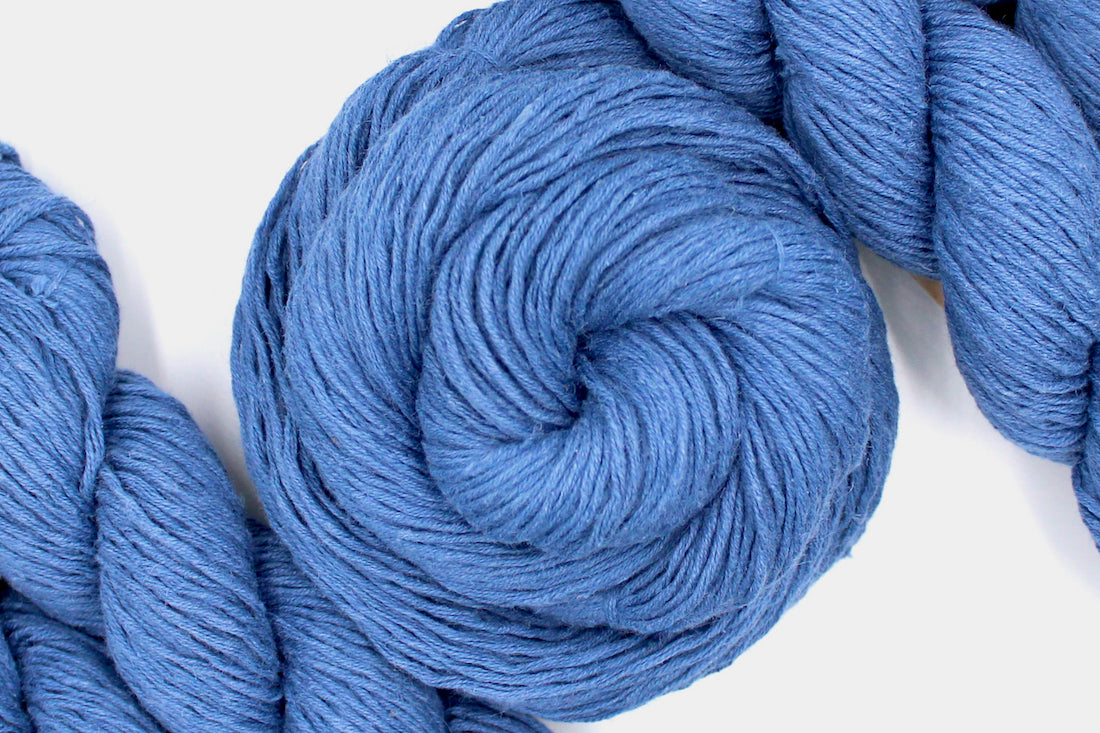 A skein of Vegan, Cornflower Blue, 55% Ramie, 45% Cotton, Worsted weight Yarn recycled by hand from unwanted sweaters swirled attractively in the center of the frame.