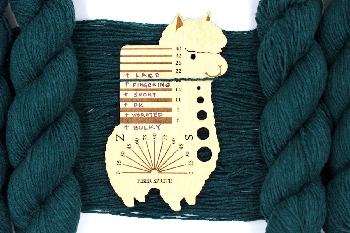 A skein of Dark Forest green, Fingering Yarn recycled by hand from unwanted sweaters draped over a Llama shaped Yarn weight tool.