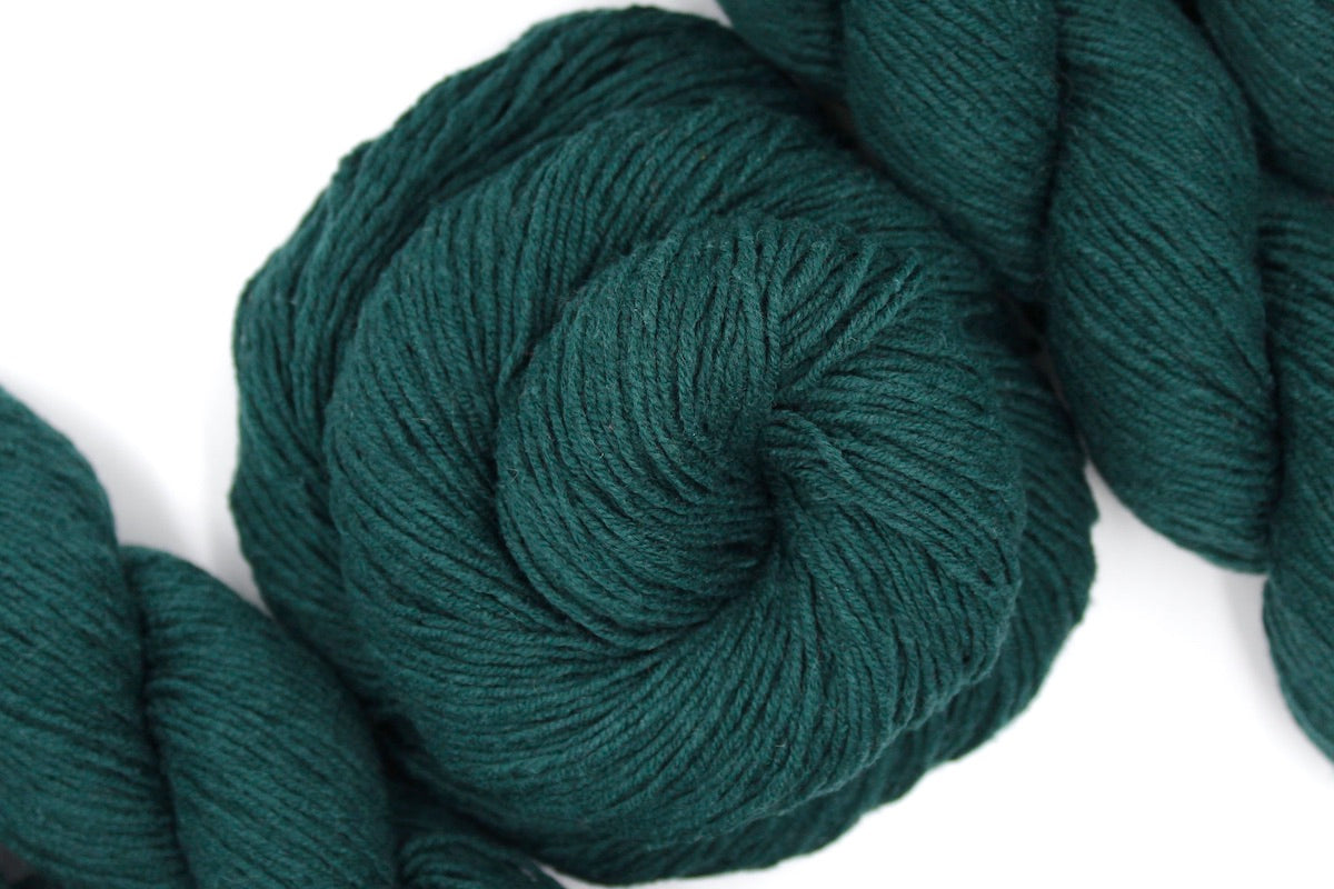 A skein of Dark Forest green, Fingering weight Yarn recycled by hand from unwanted sweaters swirled attractively in the center of the frame.