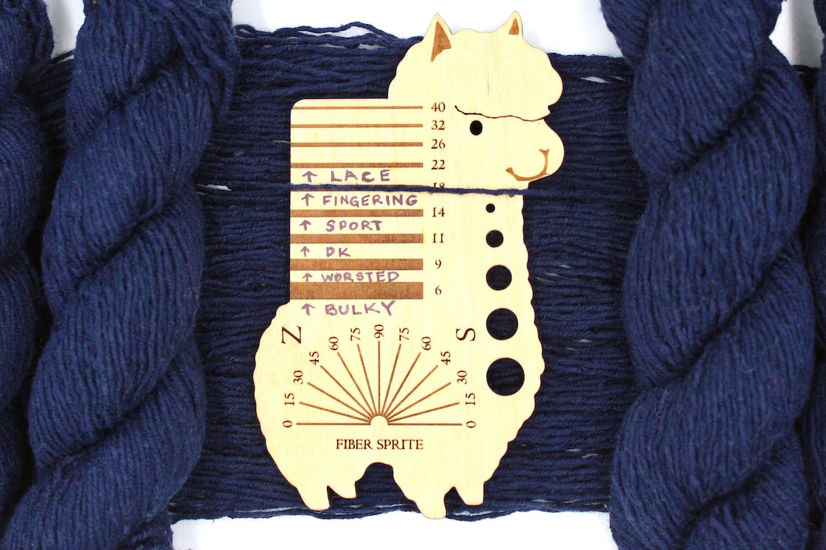 A skein of Dark Navy Blue, Fingering Yarn recycled by hand from unwanted sweaters draped over a Llama shaped Yarn weight tool.