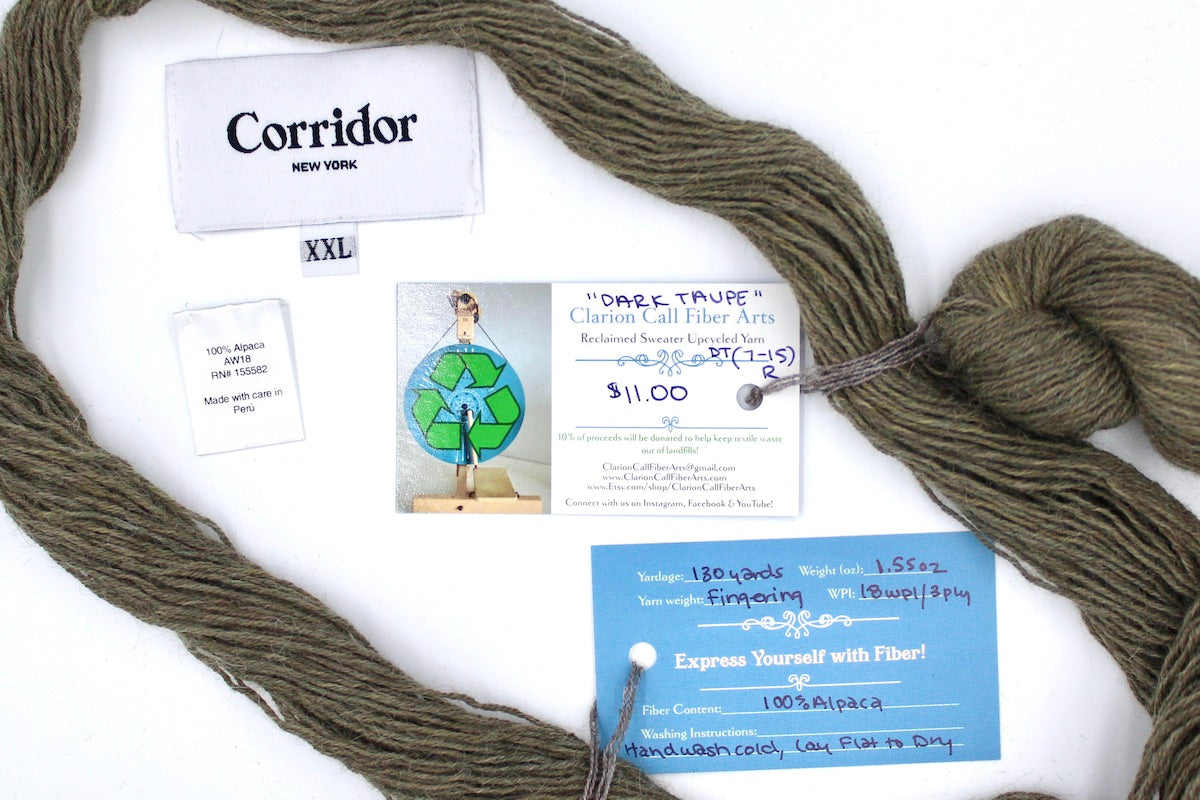 A skein of Natural Alpaca, Fingering yarn encircling the sweater labels it was recycled from, as well as the hand written yarn tags detailing the specs of this upcycled yarn to help you make your next project!
