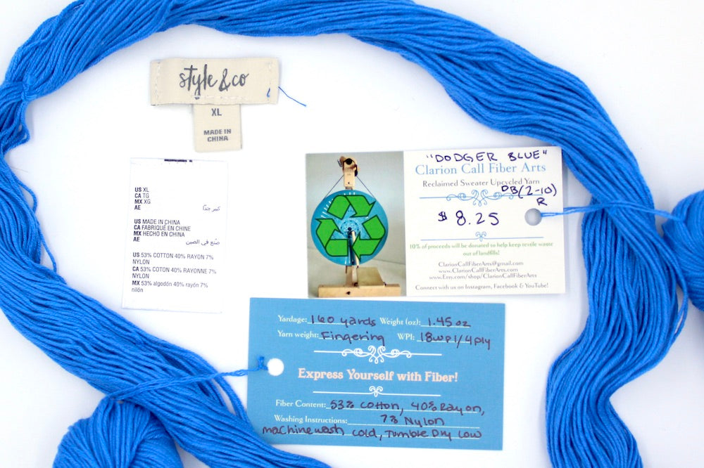 A skein of Baby Blue, Cotton Rayon Nylon, Fingering Weight yarn encircling the sweater labels it was recycled from, as well as the hand written yarn tags detailing the specs of this upcycled yarn to help you make your next project!