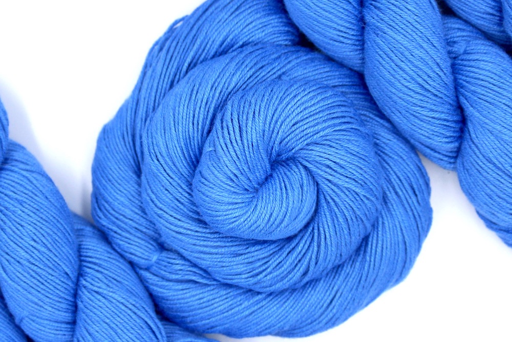 A skein of Baby Blue, Cotton Rayon Nylon, Fingering weight Yarn recycled by hand from unwanted sweaters swirled attractively in the center of the frame.