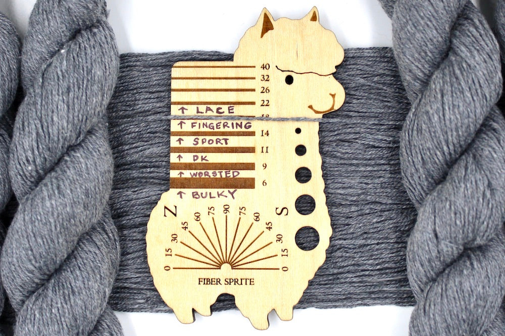 A skein of Light Grey, Cotton Viscose, Fingering Weight Yarn recycled by hand from unwanted sweaters draped over a Llama shaped Yarn weight tool.