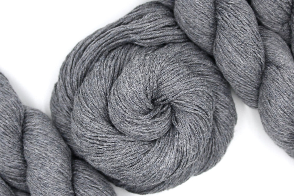 A skein of Light Grey, Cotton Viscose, Fingering weight Yarn recycled by hand from unwanted sweaters swirled attractively in the center of the frame.