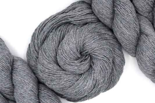 A skein of Light Grey, Cotton Viscose, Fingering weight Yarn recycled by hand from unwanted sweaters swirled attractively in the center of the frame.