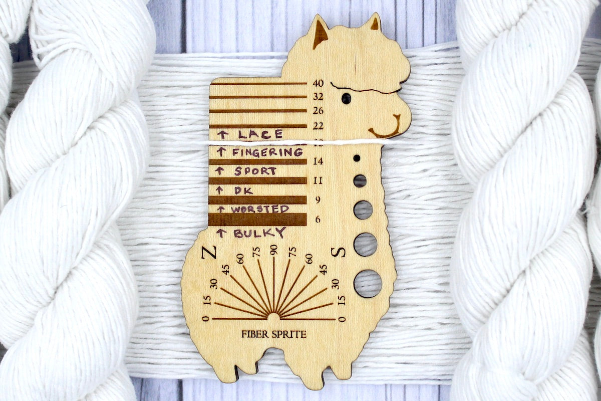 A skein of Pure White, Cotton, Fingering Weight Yarn recycled by hand from unwanted sweaters draped over a Llama shaped Yarn weight tool.
